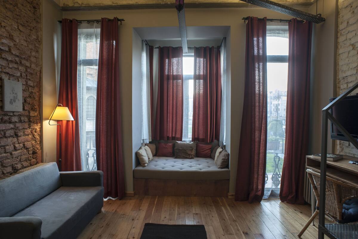 A cozy room with a sofa, a window seat with curtains, a lamp, and a television.