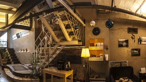 Un loft espacioso con techo alto, vigas a la vista, una escalera, una máquina de café, un tocadiscos y una zona de estar acogedora con un gato.