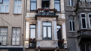 Un edificio histórico con detalles arquitectónicos ornamentales, que incluyen un balcón y marcos de ventanas decorativos.