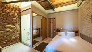 Un dormitorio con pared de ladrillo, techo de madera, cama con ropa blanca y armario de madera.