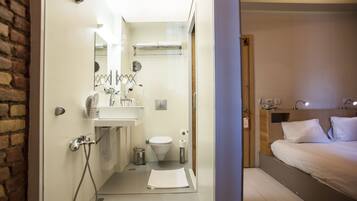 Habitación de hotel pequeña con ducha, inodoro y cama.