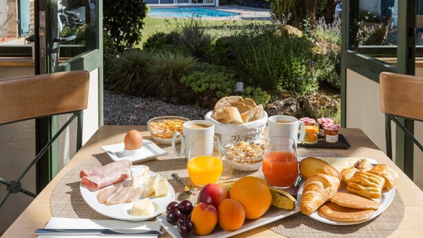 A breakfast table with various food items and a view of a swimming pool and greenery. - Domaine Le Martinet, The Originals Relais  (Bouin)