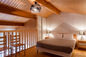 A wooden cabin bedroom with a bed, two bedside tables with lamps, a wooden chair, and a sloped ceiling with a hanging light fixture. - Domaine Le Martinet, The Originals Relais  (Bouin)