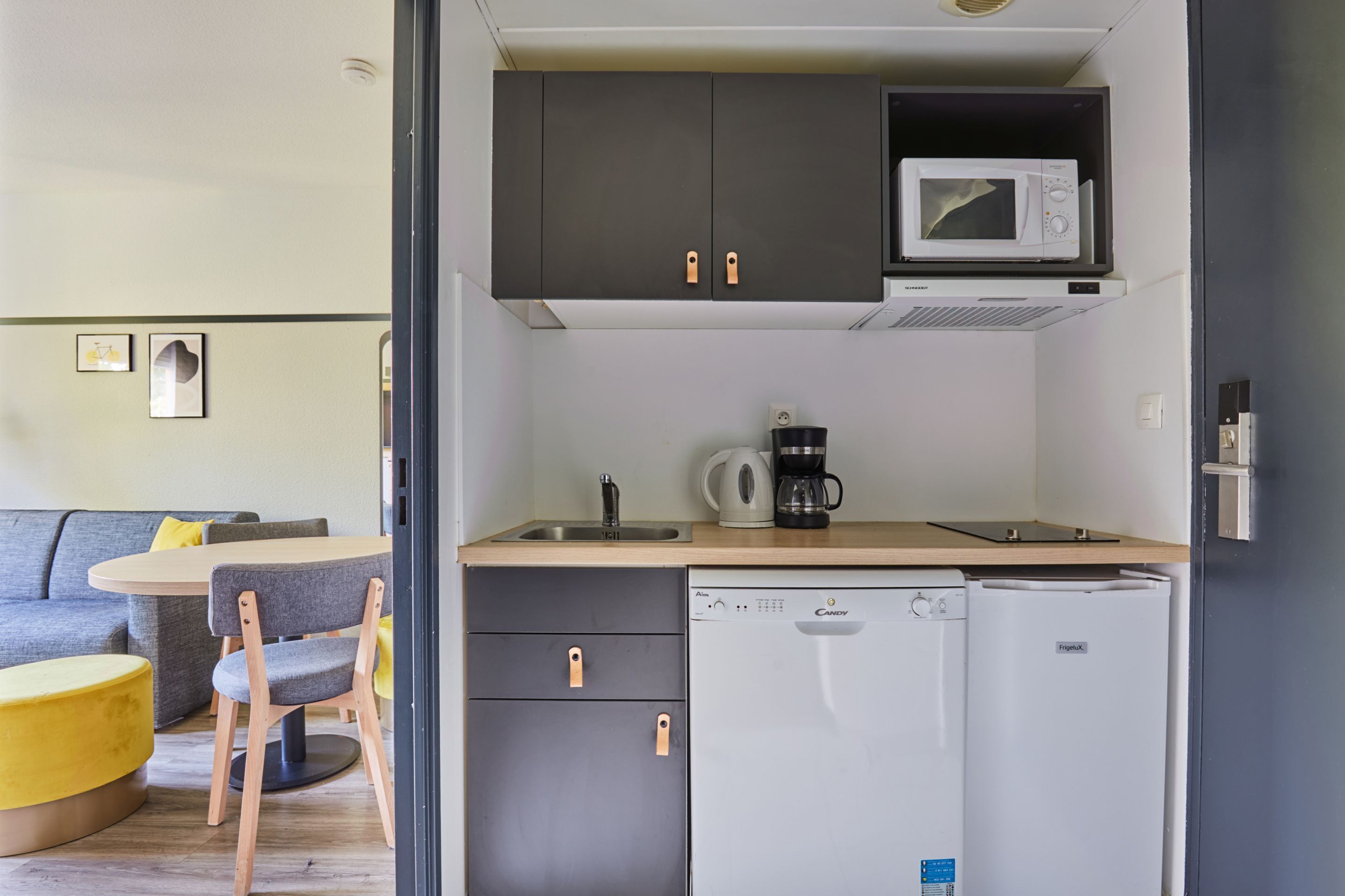 Une cuisine compacte équipée d’un four à micro-ondes, d’une machine à café et d’un réfrigérateur. Un coin repas avec une table et des chaises est également à disposition.