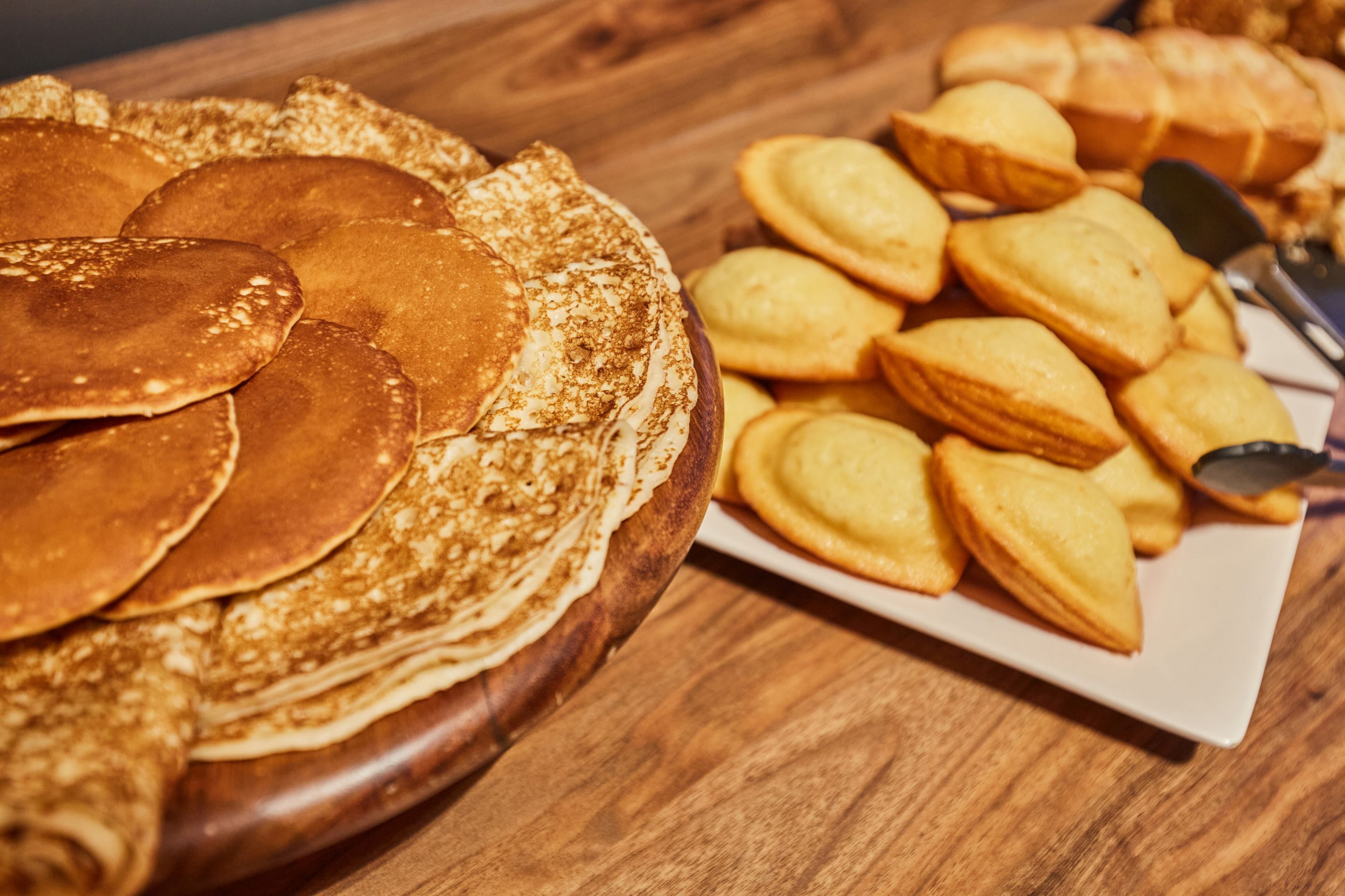 Una mesa de madera con una pila de tortitas y un plato de galletas con forma de corazón.
