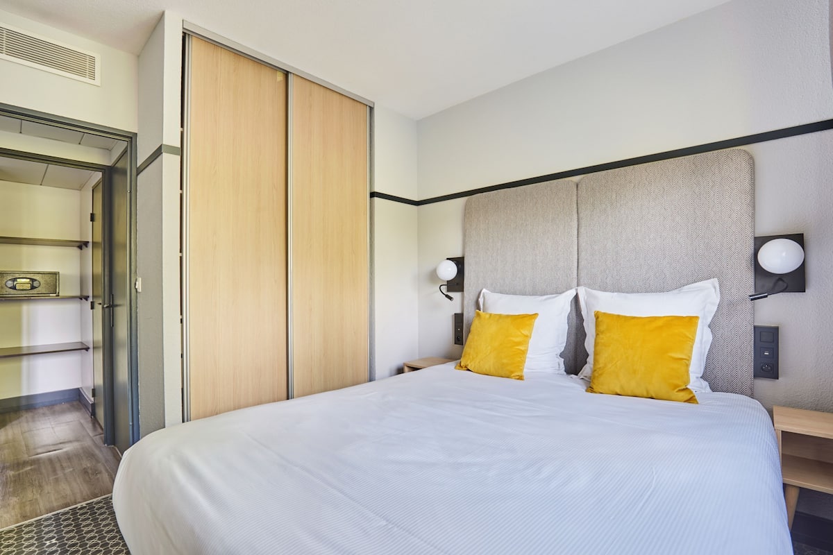 Ein modernes Hotelzimmer mit einem großen Bett, einem Holzschrank und einem Nachttisch mit einer Lampe.