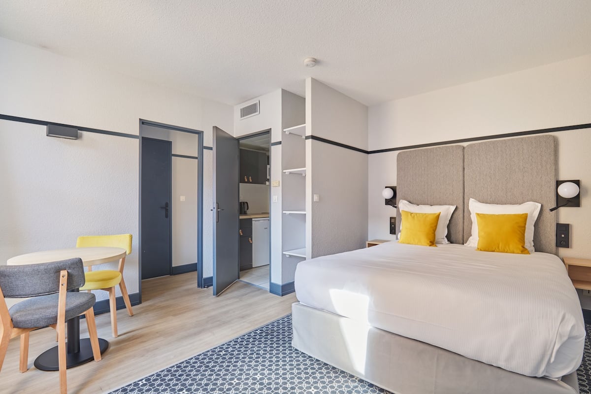 Ein Hotelzimmer mit einem Bett, einem Schreibtisch mit Stühlen, einem Kleiderschrank und einer kleinen Küchenzeile.
