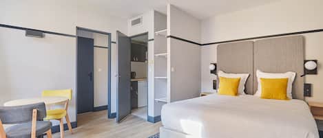 A hotel room with a bed, a desk with chairs, a wardrobe, and a small kitchenette.