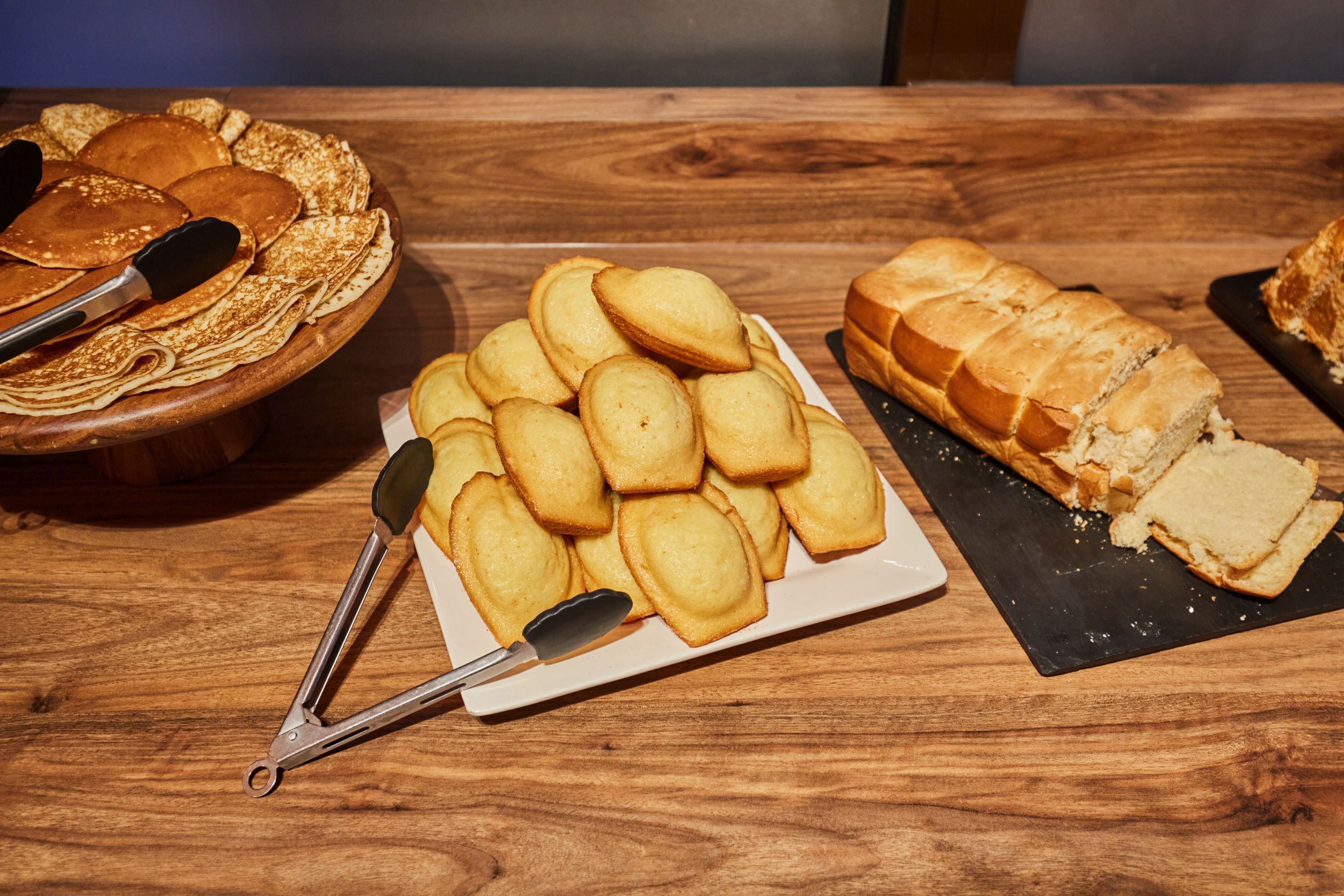 Ein Holztisch mit einem Teller Kekse, einem Brotlaib und einer Schüssel Pfannkuchen.