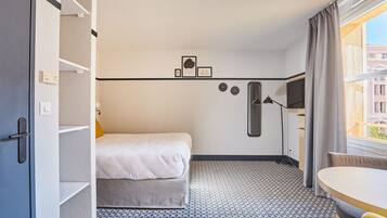 A compact hotel room with a bed, a desk, a chair, a TV, and a window with curtains.
