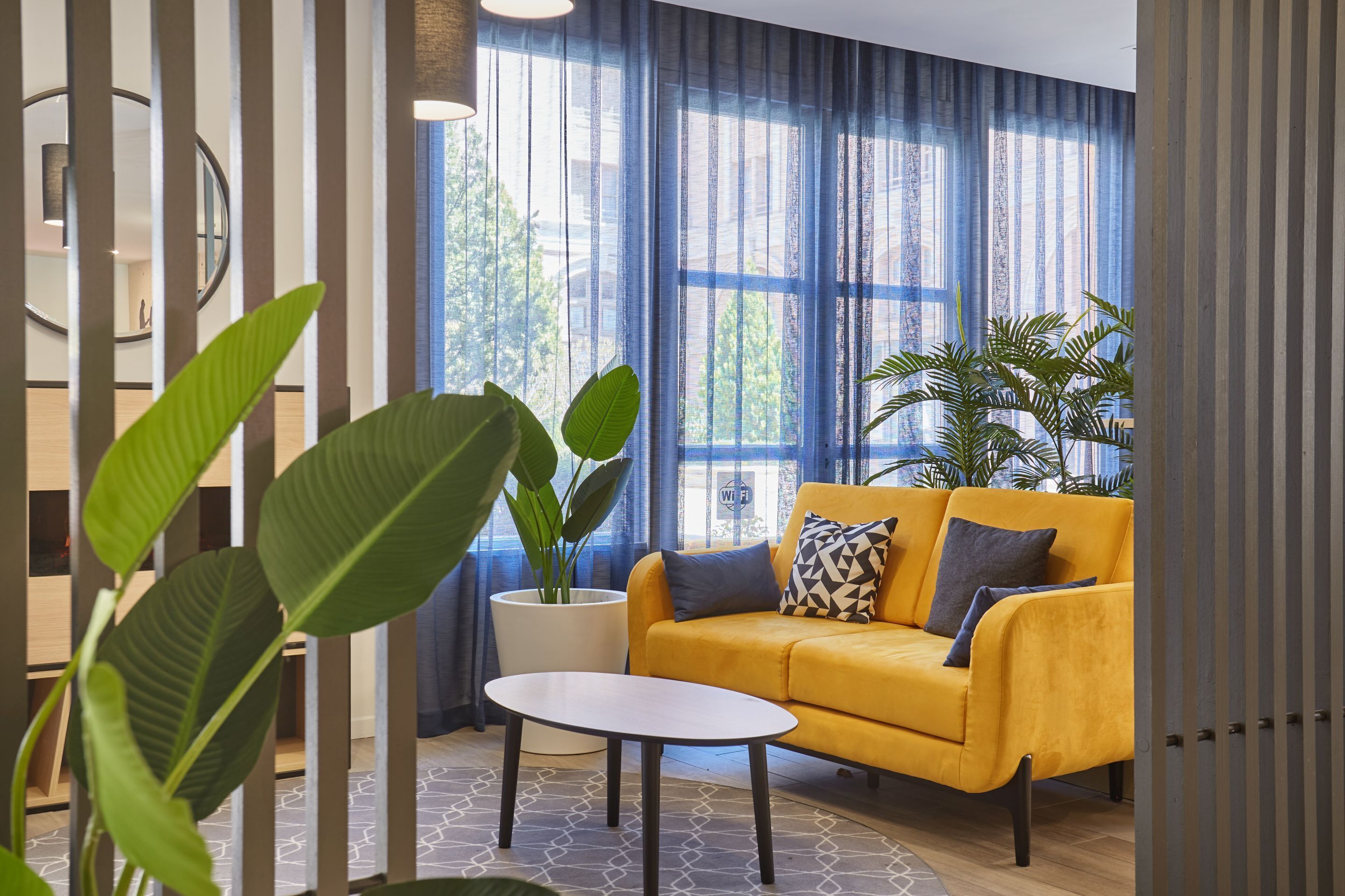 Un salon moderne avec un canapé jaune, une table basse ronde et de grandes plantes en pot.