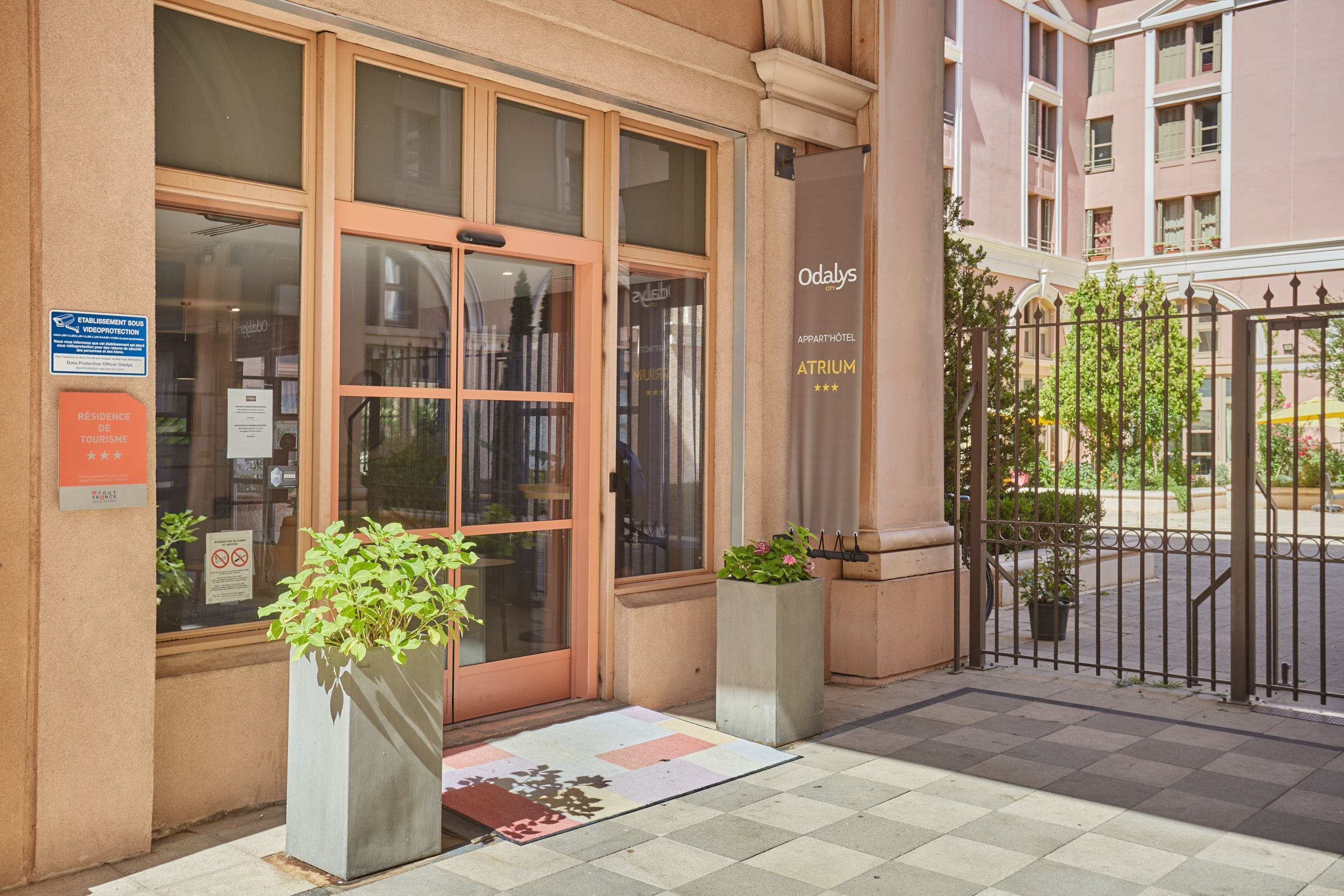 Een hotelentree met een glazen deur, een bordje voor Odalys Appartements, en een metalen hek.