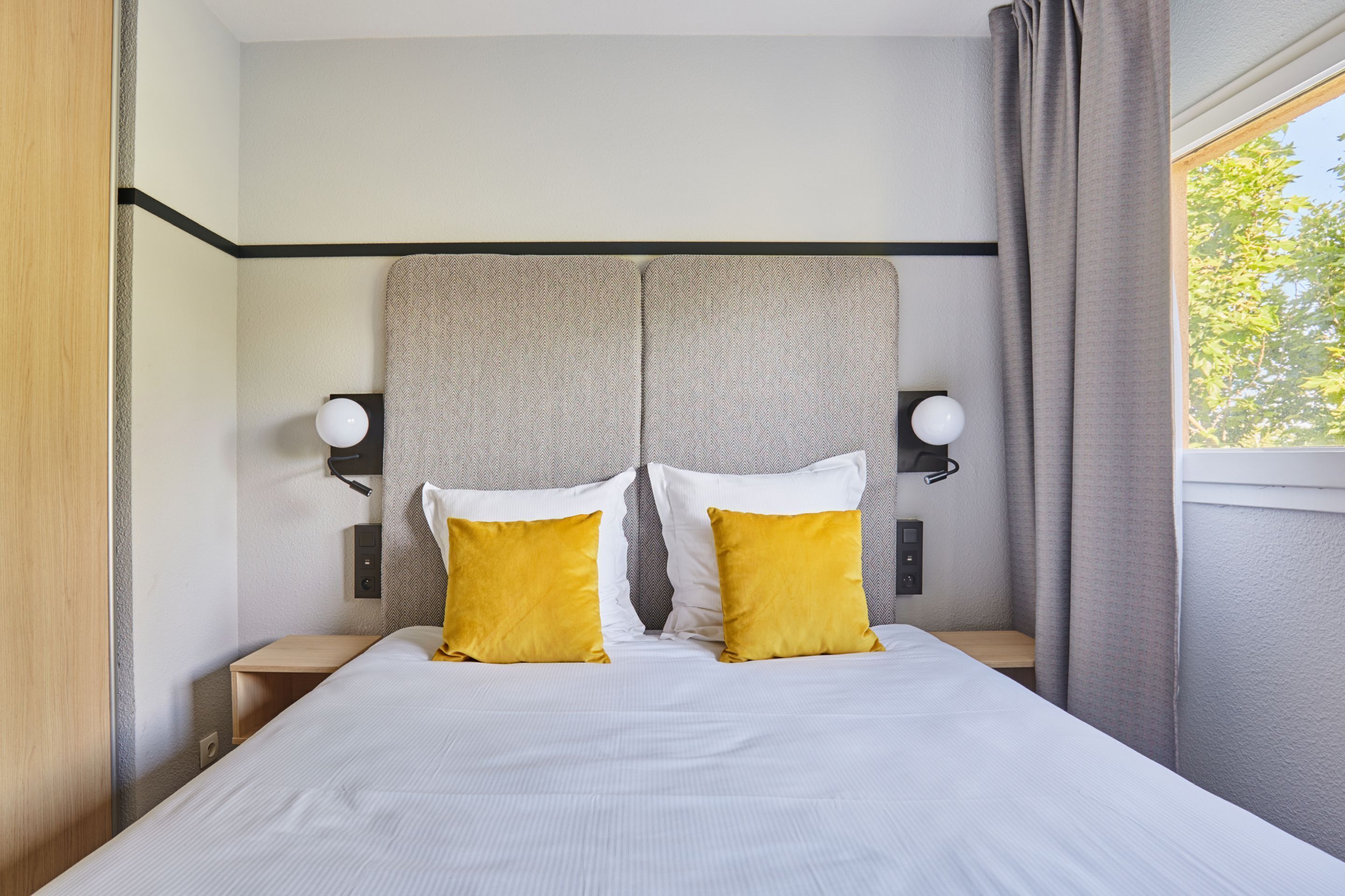 A hotel room with a large bed, two bedside tables, and a headboard with integrated lighting.