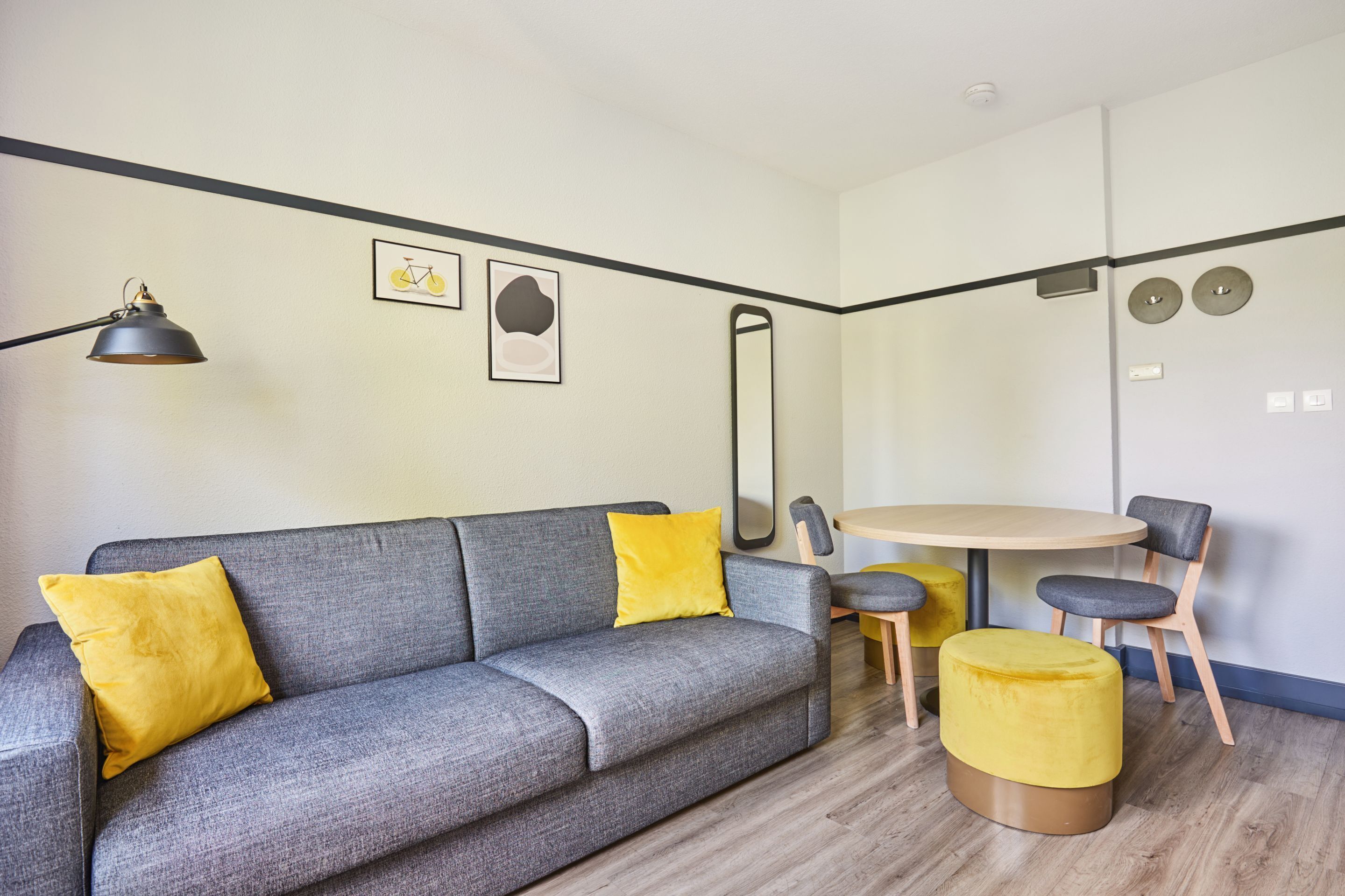 Una sala de estar moderna con un sofá gris, cojines amarillos, una mesa redonda de madera y sillas a juego.