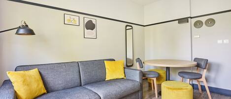 Una sala de estar moderna con un sofá gris, cojines amarillos, una mesa redonda de madera y sillas a juego.