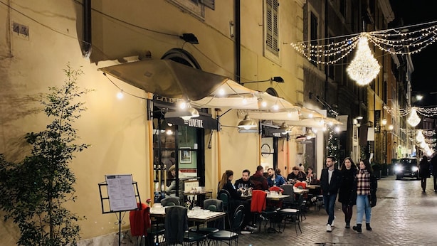 Un café al aire libre con mesas, sillas, un tablero de menú y luces colgantes.