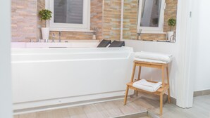 Un baño moderno con una bañera blanca, un taburete de madera con una toalla y un espejo sobre la bañera.