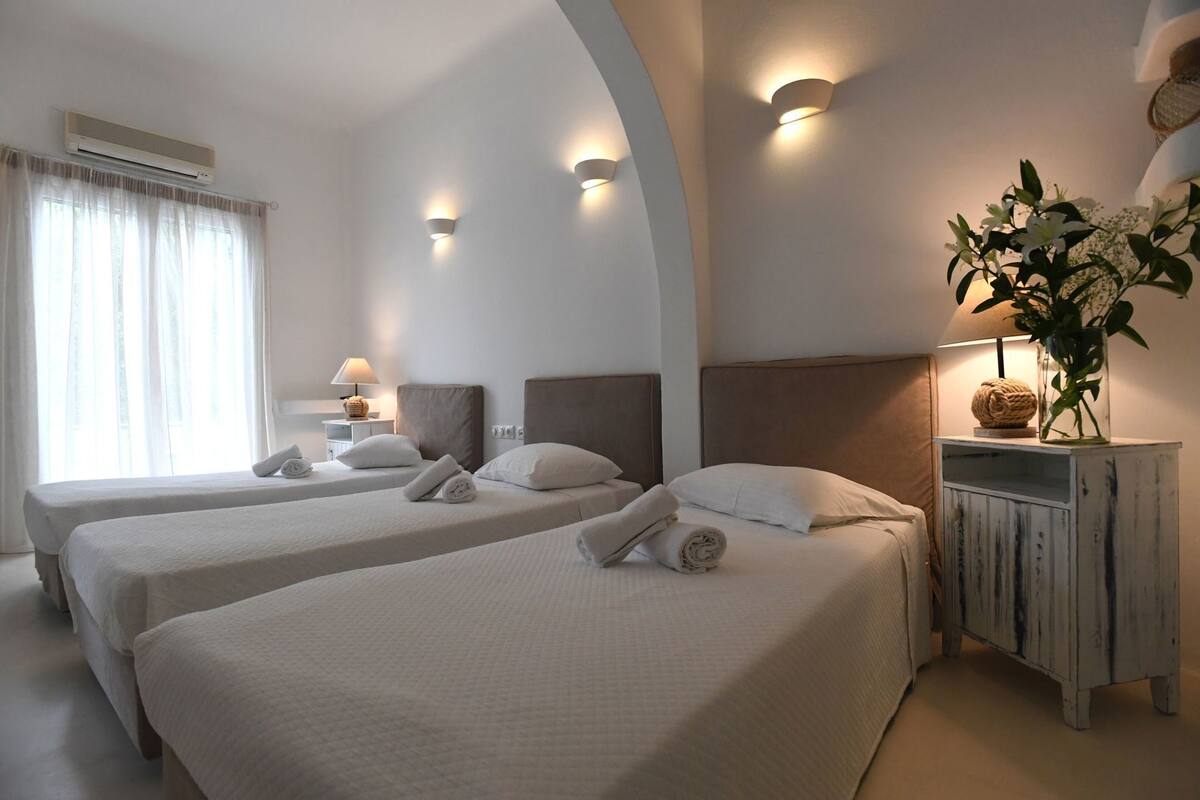 A hotel room with two beds, a nightstand, a lamp, a plant, and an air conditioning unit.