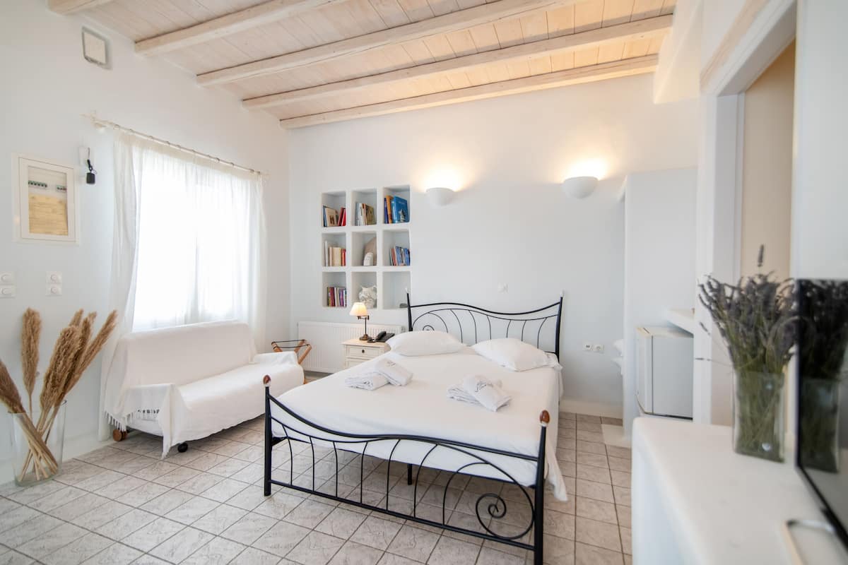 A bedroom with a bed, bedside table, lamp, bookshelves, and a window with curtains.