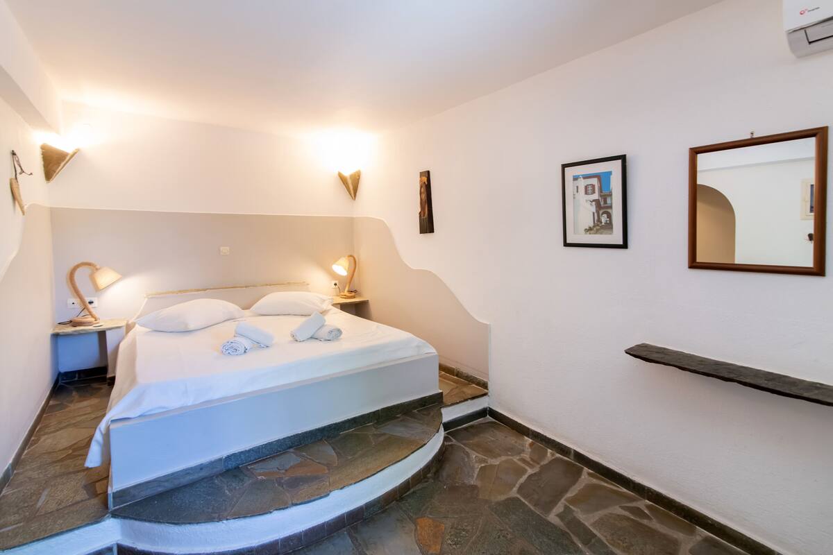 A bedroom with a bed, two bedside lamps, a framed picture, a mirror, and a stone staircase.