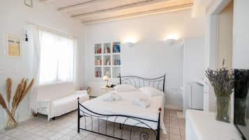 A bedroom with a bed, bedside table, lamp, bookshelves, and a window with curtains.