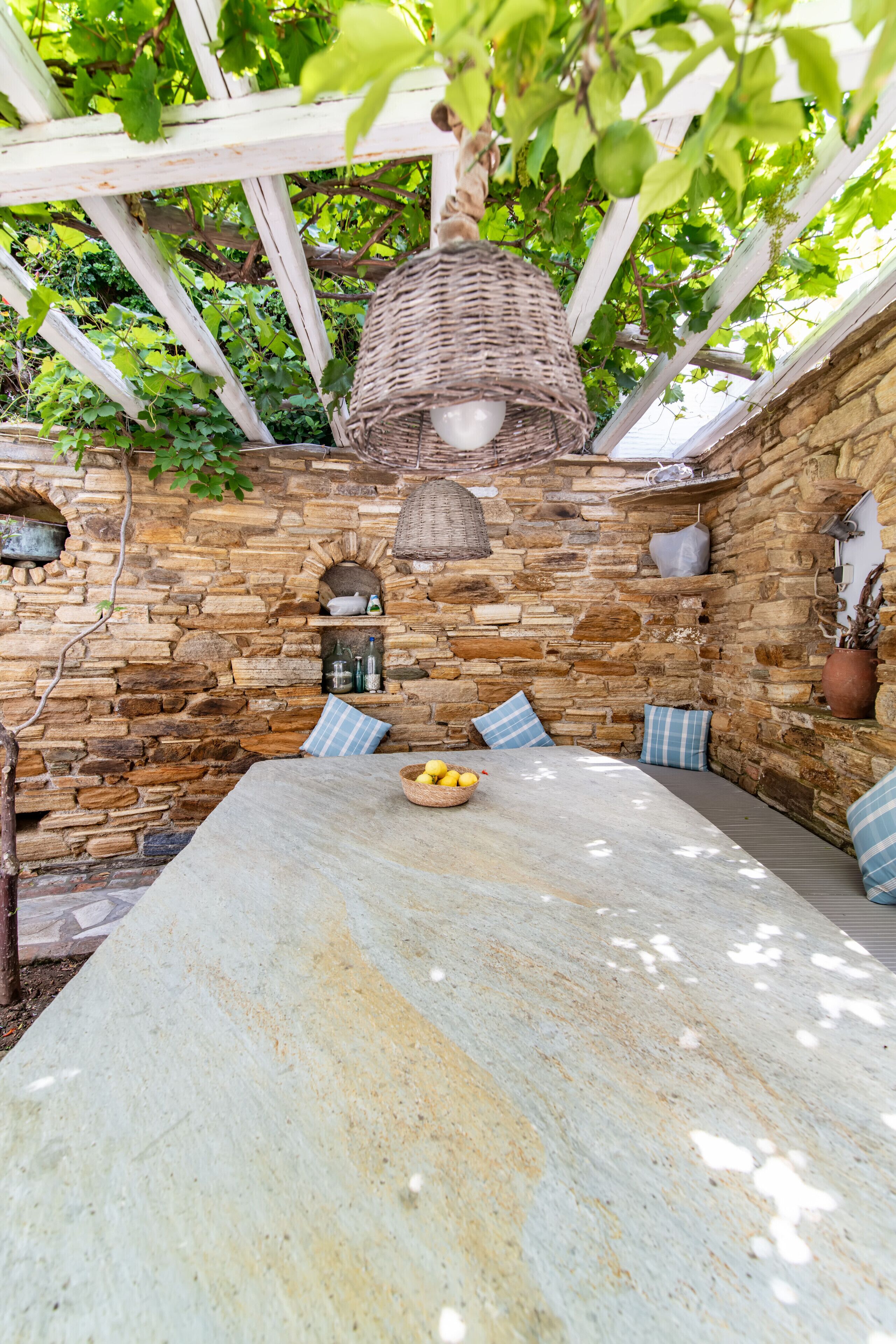 Un área de estar al aire libre con pared de piedra, lámpara colgante de mimbre y una mesa con un cuenco de limones.