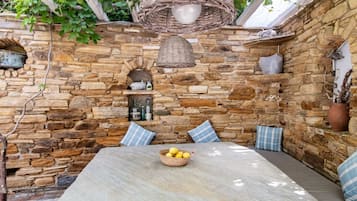 Un área de estar al aire libre con pared de piedra, lámpara colgante de mimbre y una mesa con un cuenco de limones.