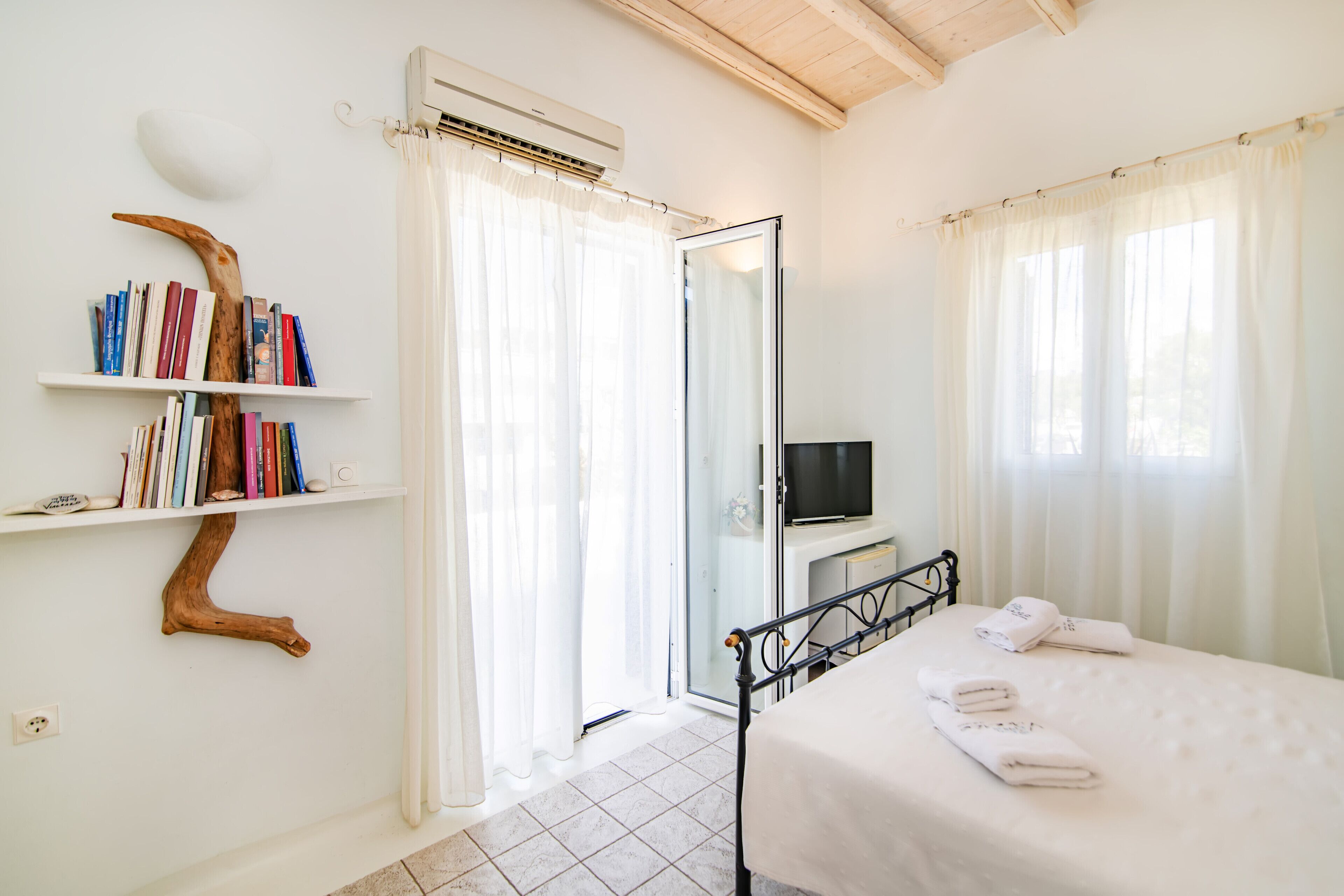 A bedroom with a bed, a TV, a bookshelf, and a door leading to another room.