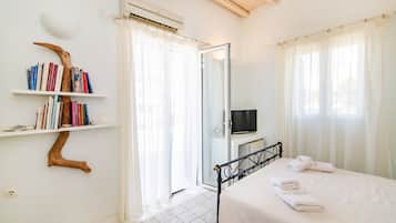 A bedroom with a bed, a TV, a bookshelf, and a door leading to another room.