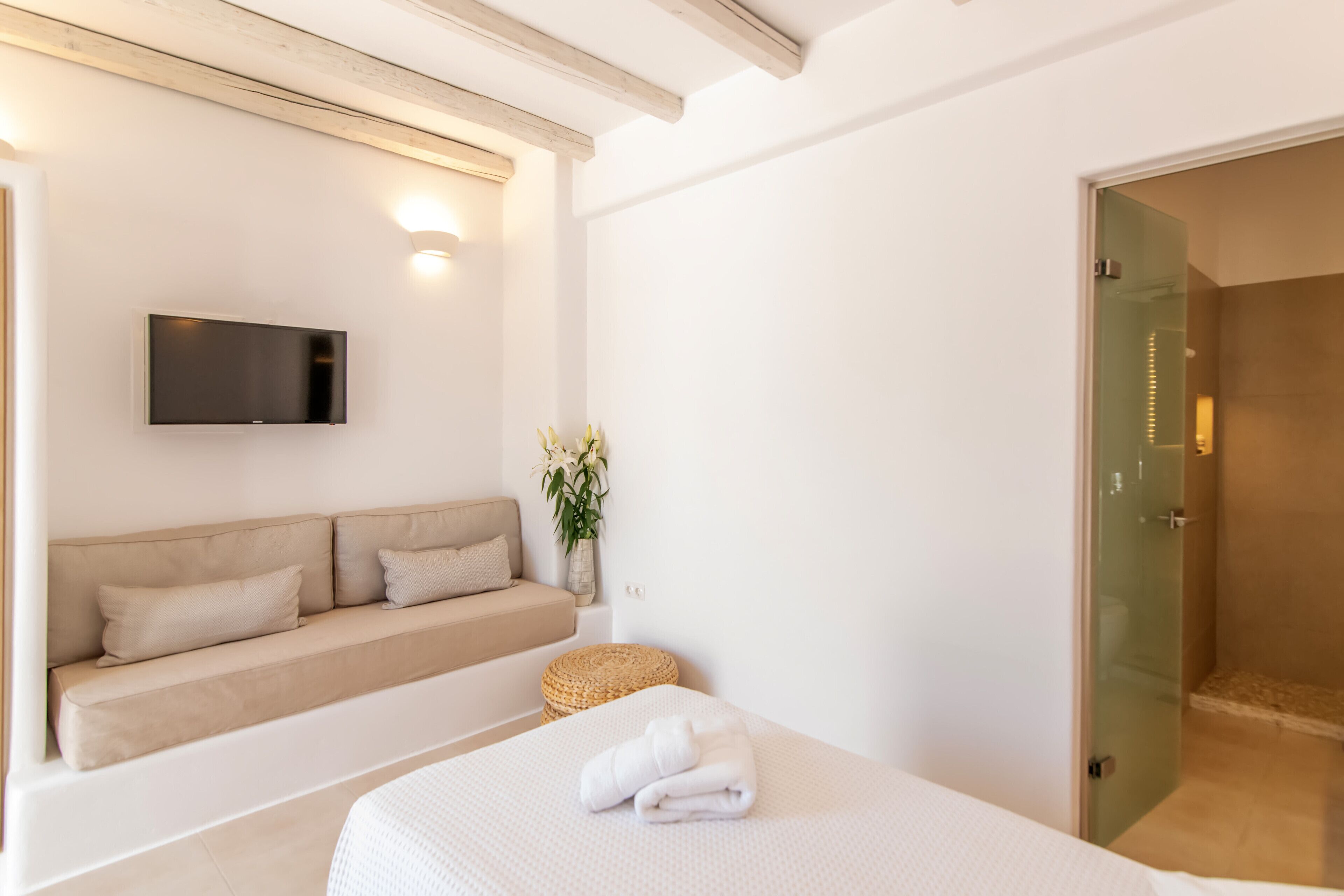 Un dormitorio moderno con cama, sofá, televisión de pantalla plana y mampara de vidrio para la ducha.