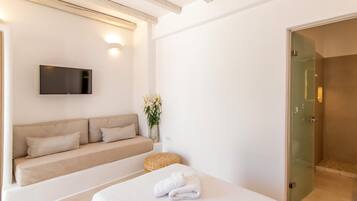Quarto moderno com cama, sofá, televisão de tela plana e box de vidro.