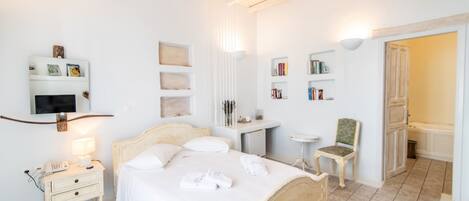 A bedroom with a bed, bedside tables, a chair, a desk, and shelves with books and decorative items.