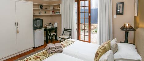 A hotel room with a bed, a desk with a television, a chair, a table with a lamp, and a view of the outdoors.