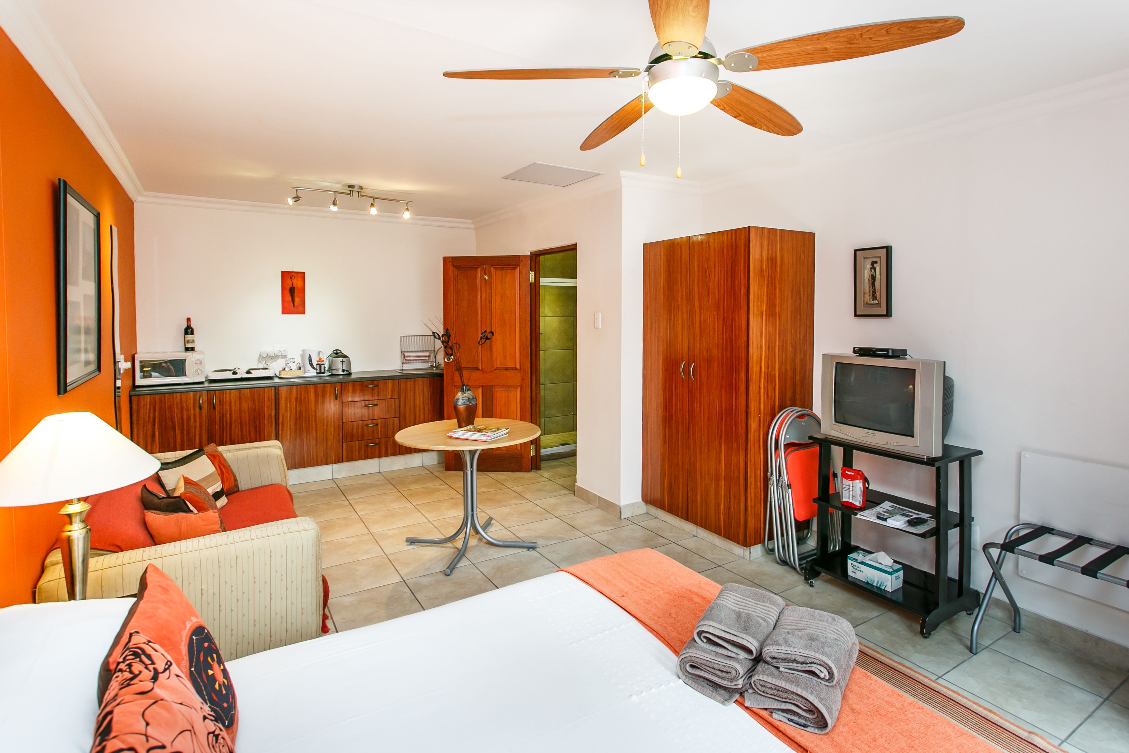 A hotel room with a bed, a desk, a chair, a TV, and a kitchenette.