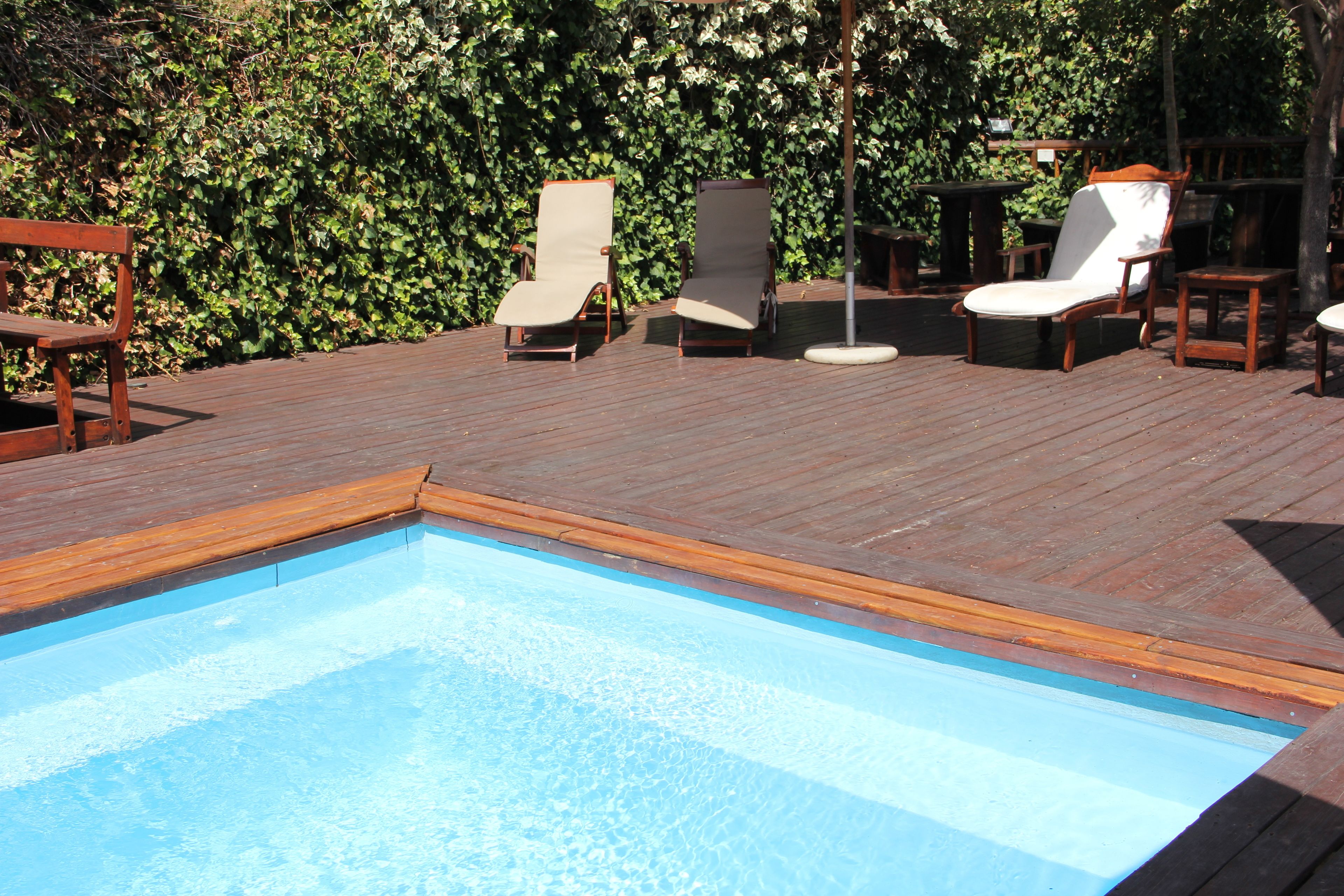Een houten terras met een zwembad, ligstoelen en een houten bank.