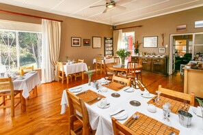 A dining area with multiple tables set for a meal, wooden chairs, and a ceiling fan. - Gumtree Guest House (Oudtshoorn)