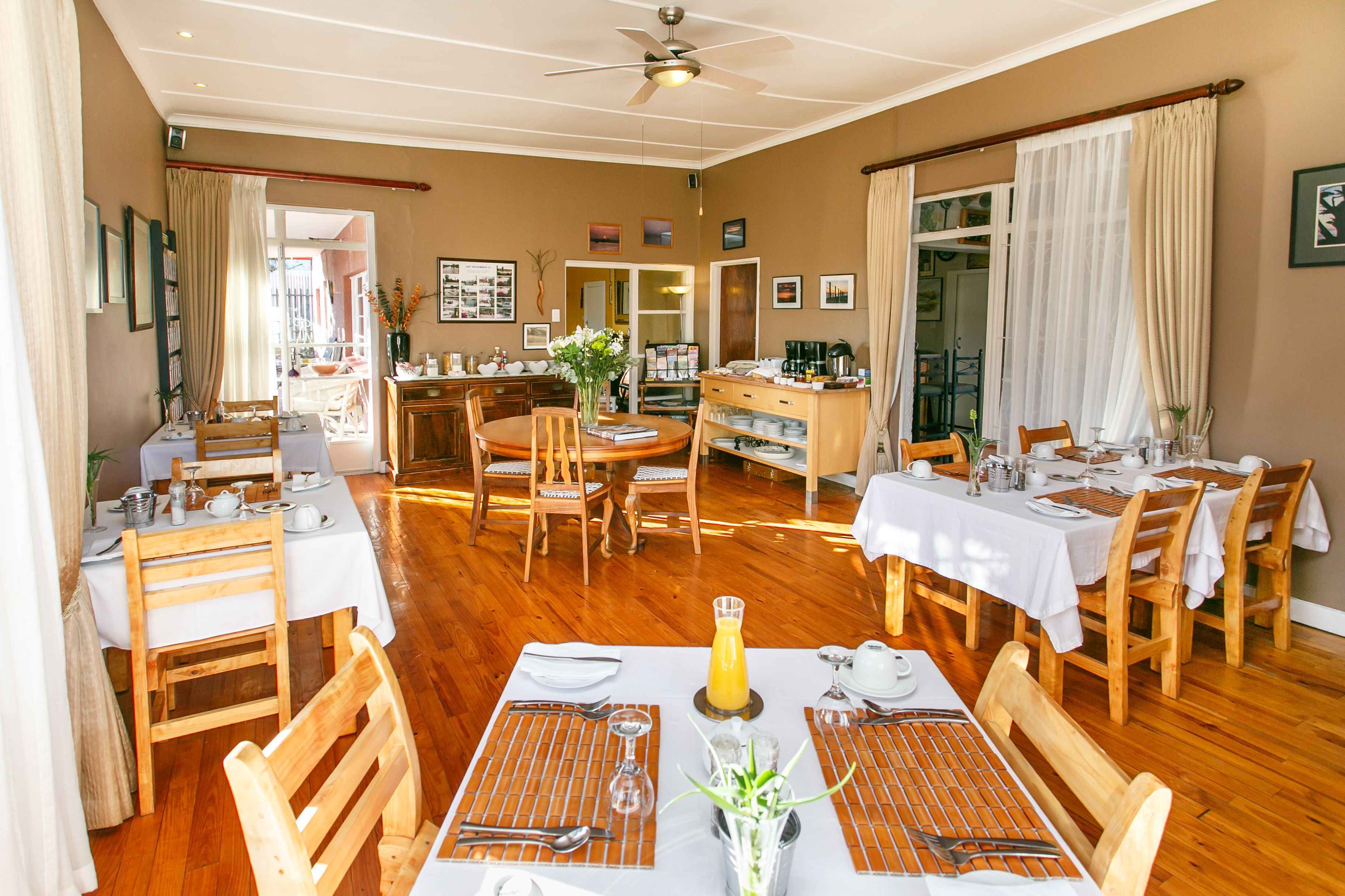 A dining area with wooden tables and chairs, white tablecloths, and a ceiling fan.