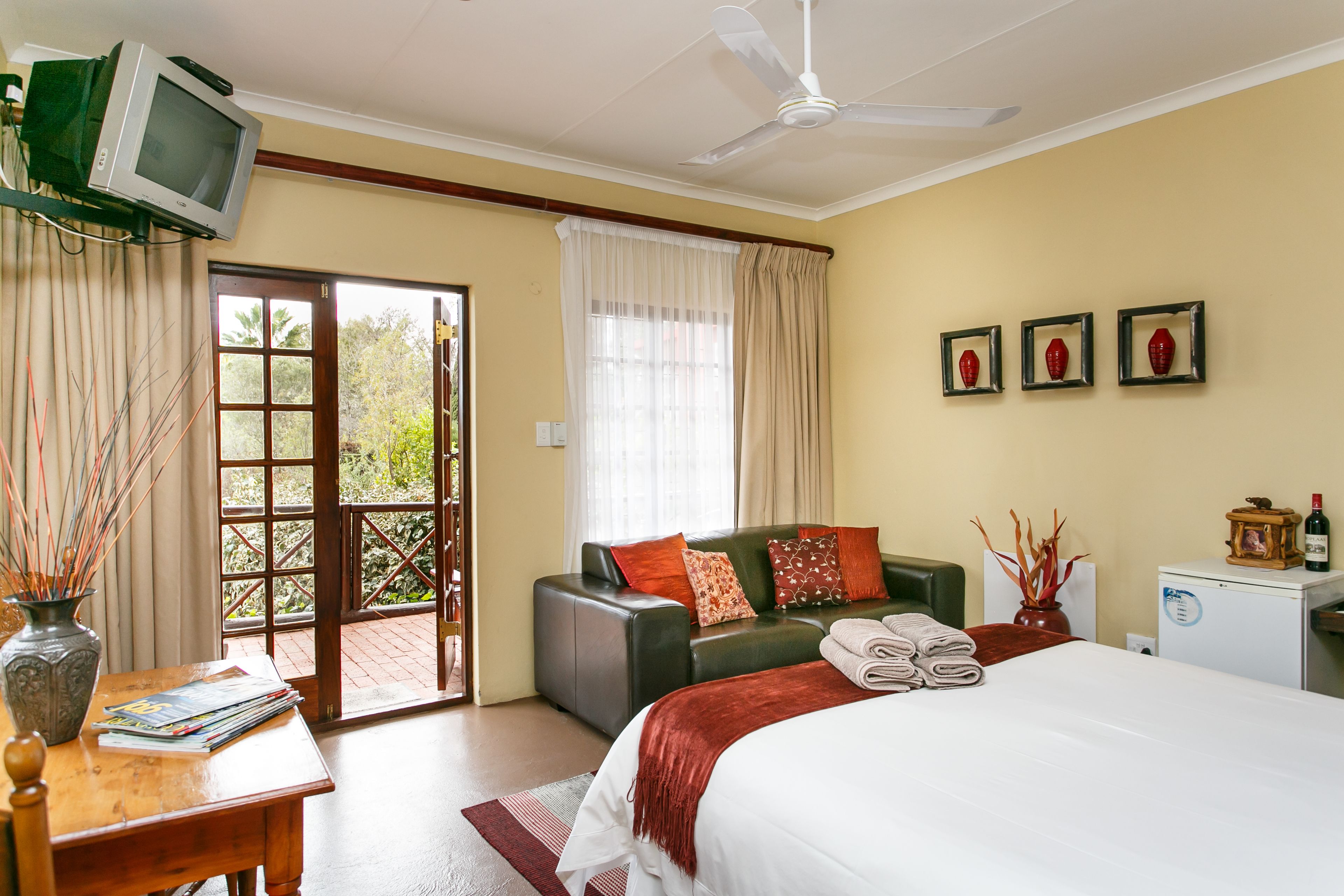 Habitación de hotel con cama, sofá, televisión, refrigerador pequeño y ventana con cortinas.
