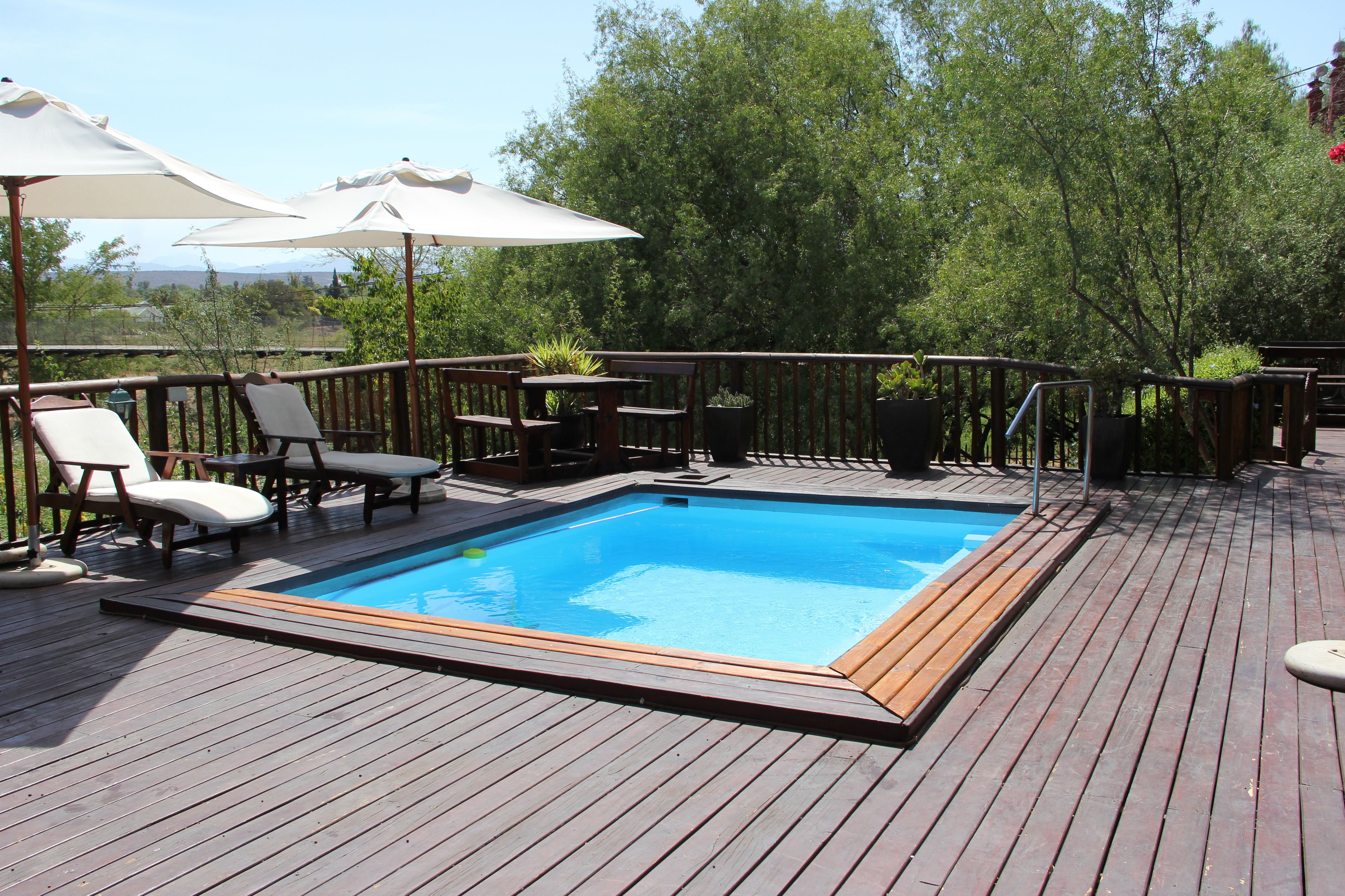 Una terraza de madera con piscina, sillas de descanso y sombrillas.