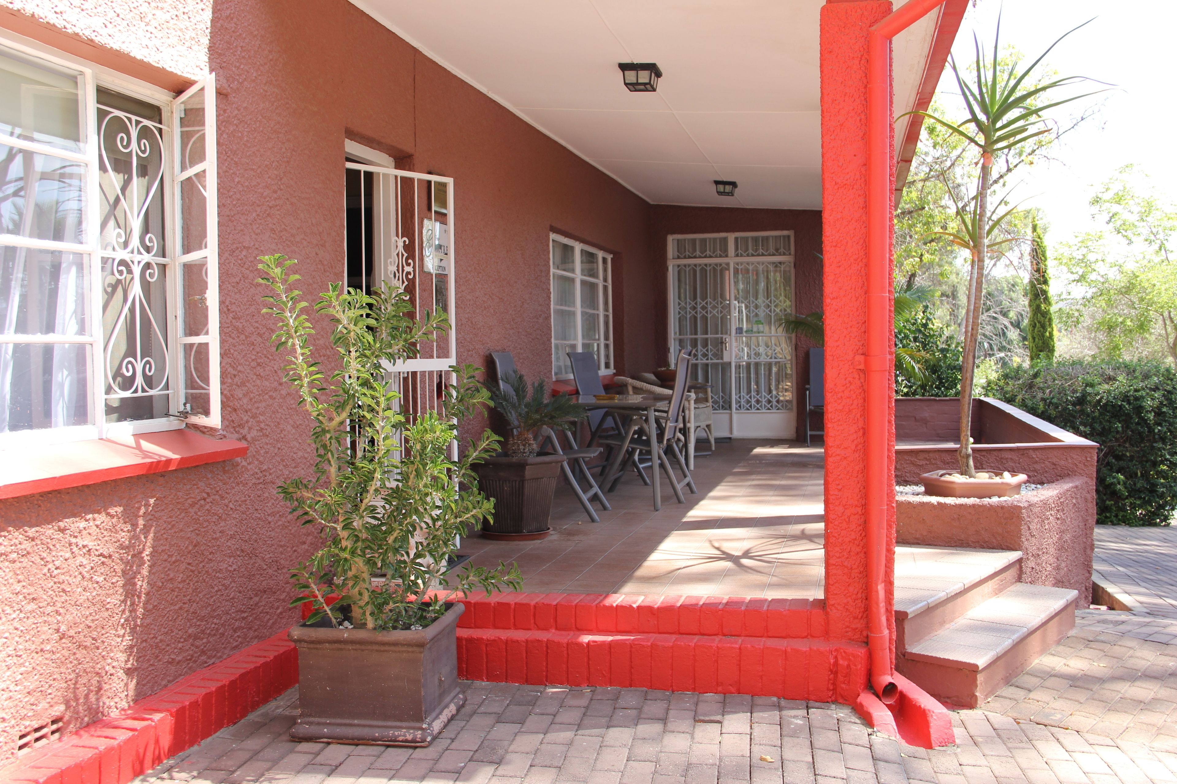 Un patio cubierto con mobiliario exterior, plantas en macetas y un borde de ladrillo rojo.