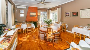 A dining area with wooden tables and chairs, a fireplace, and framed artwork on the walls. - Gumtree Guest House (Oudtshoorn)