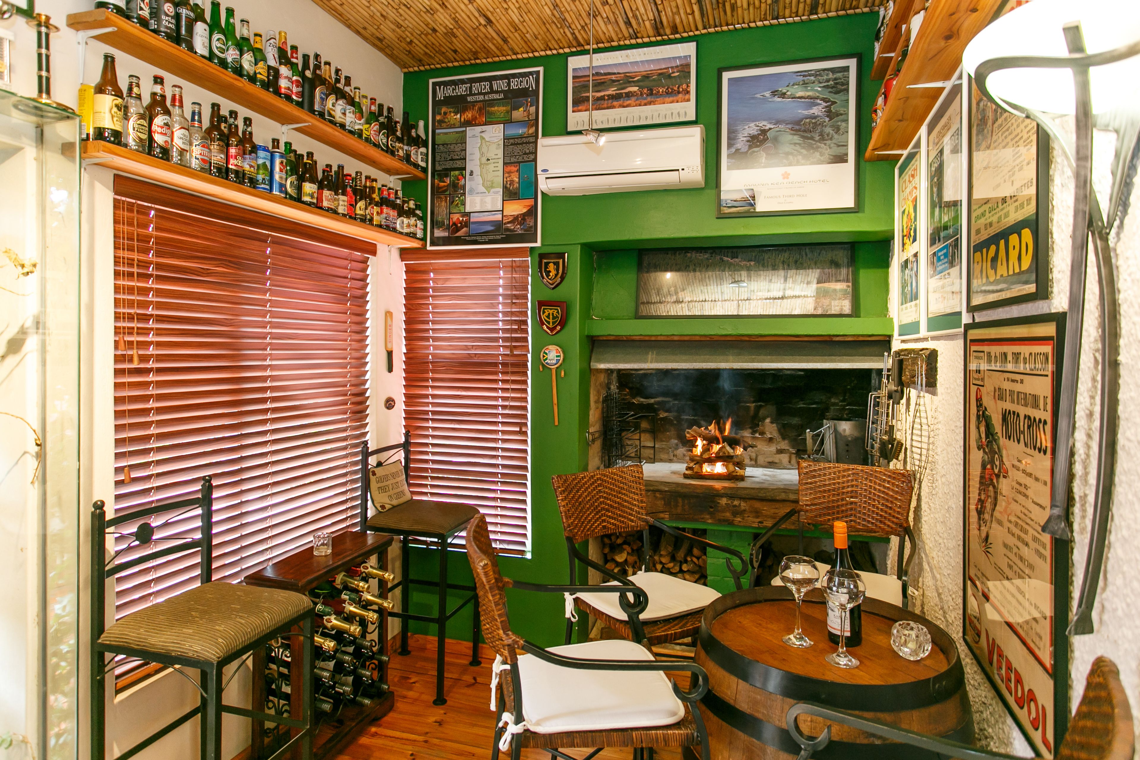 Een bar met houten flessenplanken, een open haard en een groene wand met verschillende posters.