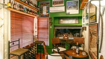 Een bar met houten flessenplanken, een open haard en een groene wand met verschillende posters.