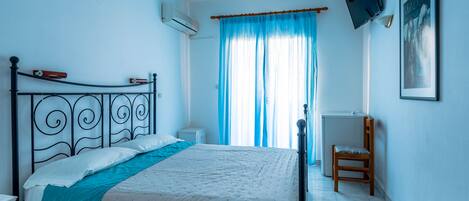 A bedroom with a bed, a chair, a TV, and a window with curtains.