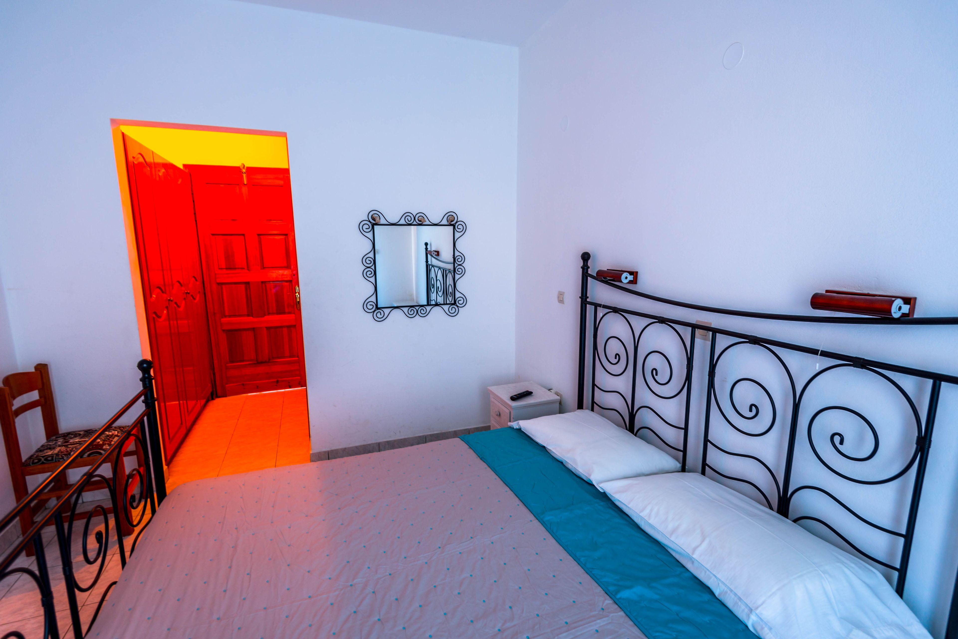 Un dormitorio con cama, una silla, una mesita de noche, un espejo y una puerta roja.