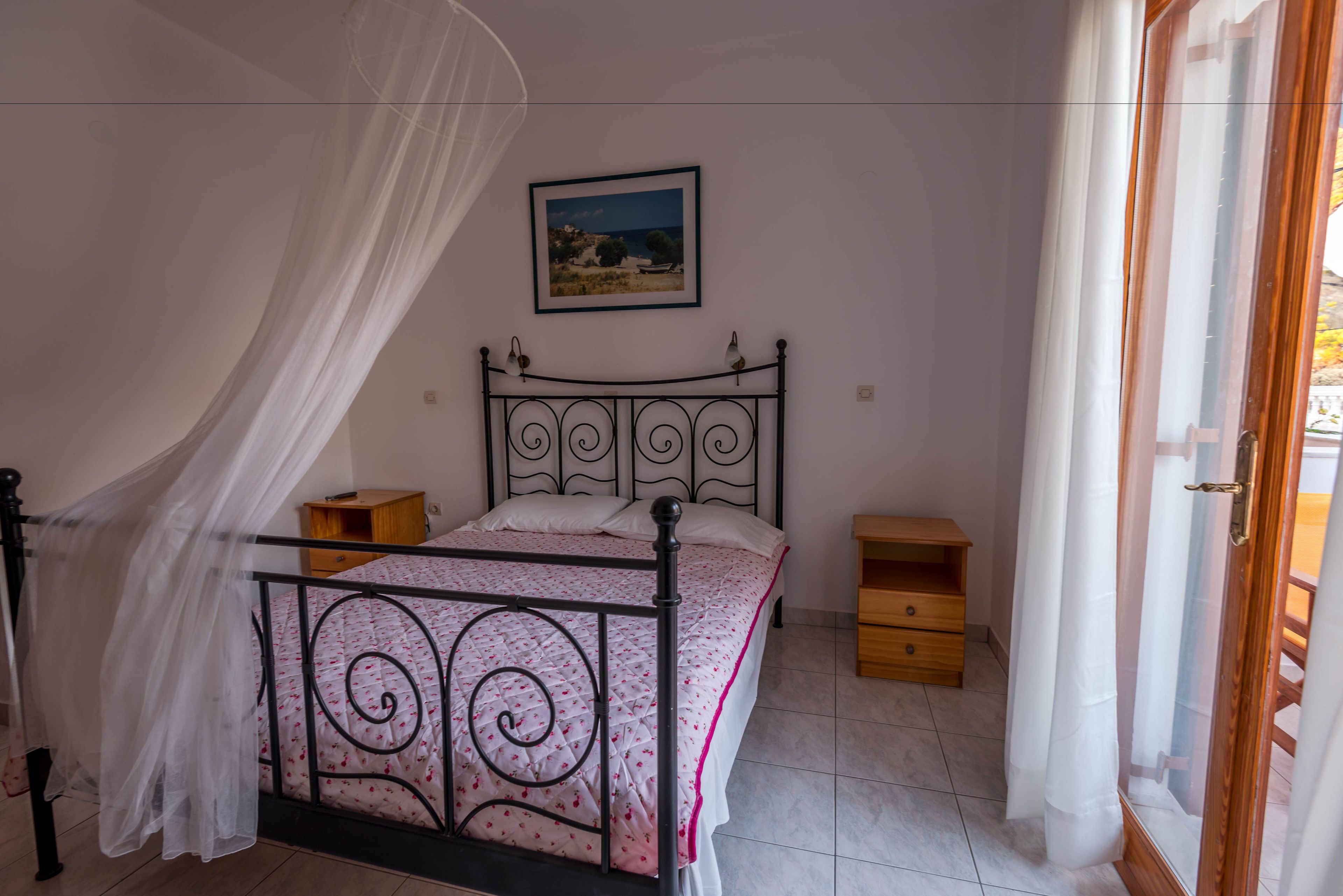 A bedroom with a bed, a bedside table, a nightstand, a wooden cabinet, and a window with curtains.