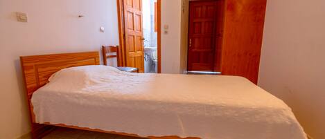 Un dormitorio con una cama de madera, una silla y una puerta que da a un baño.