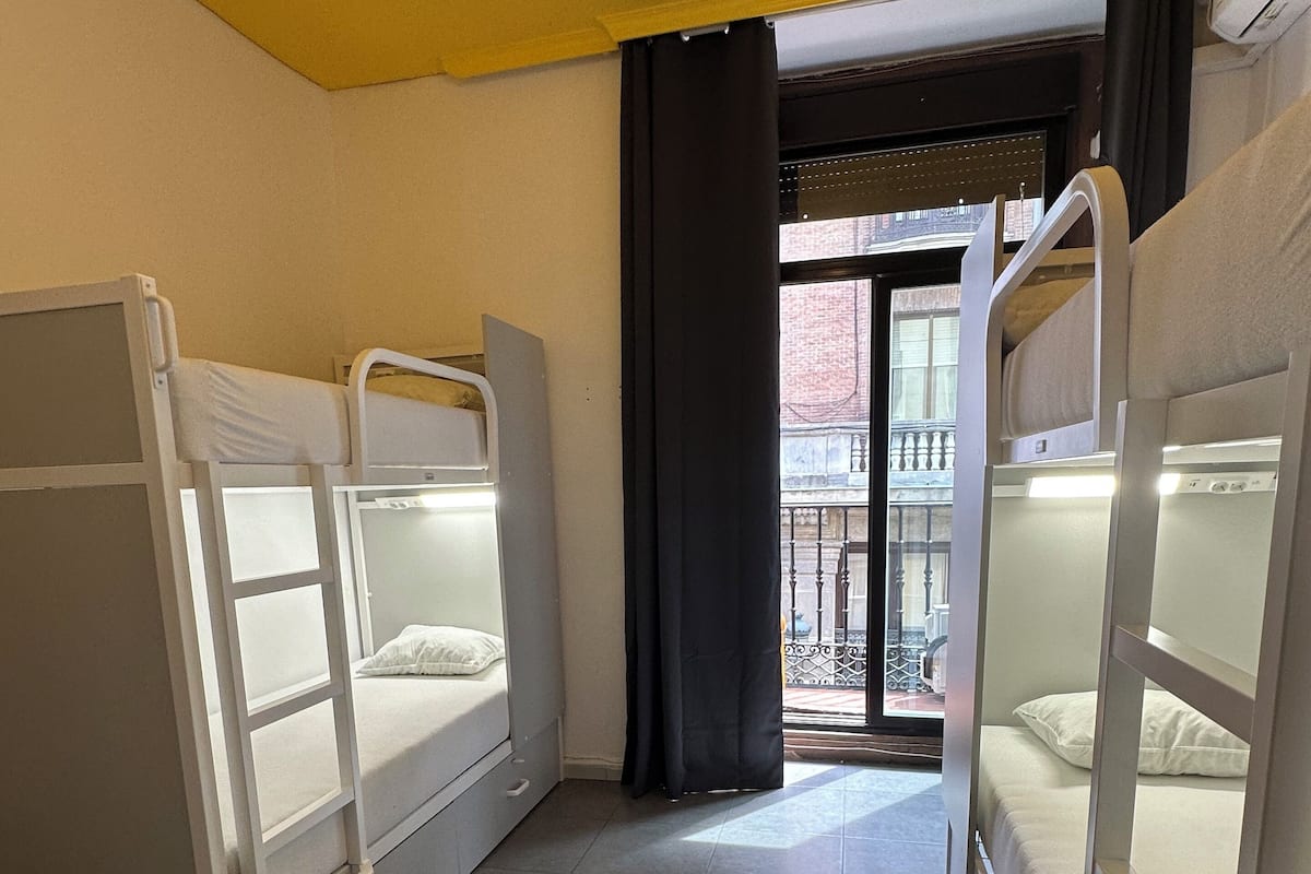 A dormitory room with bunk beds, a sliding door leading to a balcony, and a tiled floor.