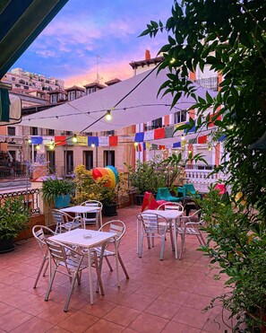 Une terrasse extérieure avec des tables et des chaises, entourée de plantes en pot et de décorations colorées.