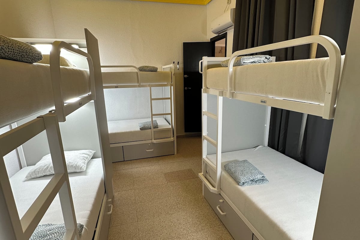 A room with bunk beds, a ceiling light, a door, and a window with curtains.